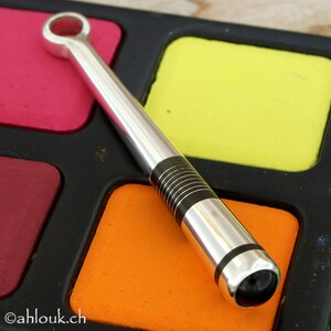 May include: A silver and black metal pipe with a round opening at one end. The pipe is lying on a black surface with colorful squares.