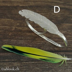 May include: Silver feather ring with a double band design. The ring is made of sterling silver and features a detailed feather design.
