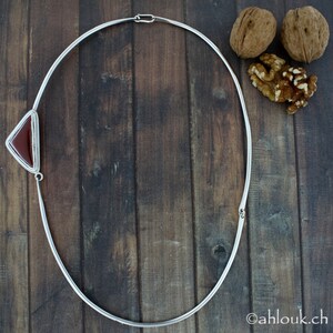 Peut inclure: Un collier ras de cou argent&eacute; avec un pendentif en forme de triangle en pierre de cornaline. Le collier est sur un fond en bois.
