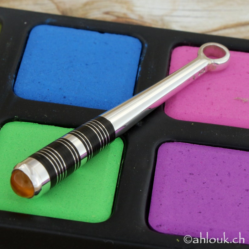 May include: A silver baseball bat pendant with a black and white striped design and a clear amber stone at the end. The pendant is on a colorful background.