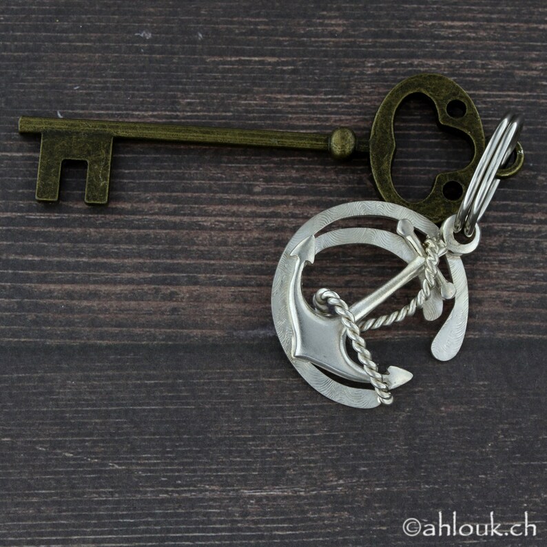 May include: A silver anchor charm attached to a key with a brass keyhole and a brass ring. The anchor charm has a rope design and is attached to the key with a silver ring.