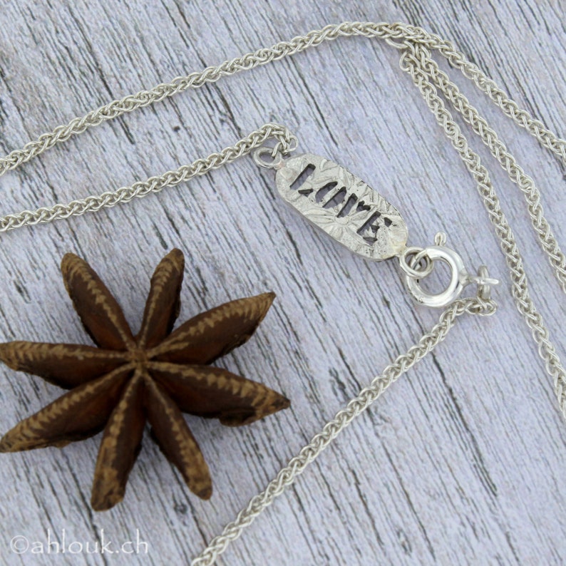 May include: A silver chain necklace with a pendant that says "LOVE" in a textured, cutout font. The pendant is attached to the chain with a silver clasp.