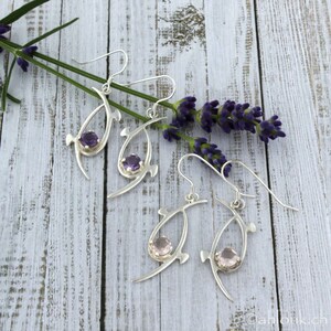 Pu&ograve; includere: Un paio di orecchini d'argento con delicati disegni di forma organica. Un orecchino presenta una pietra preziosa viola, mentre l'altro presenta una pietra preziosa rosa.