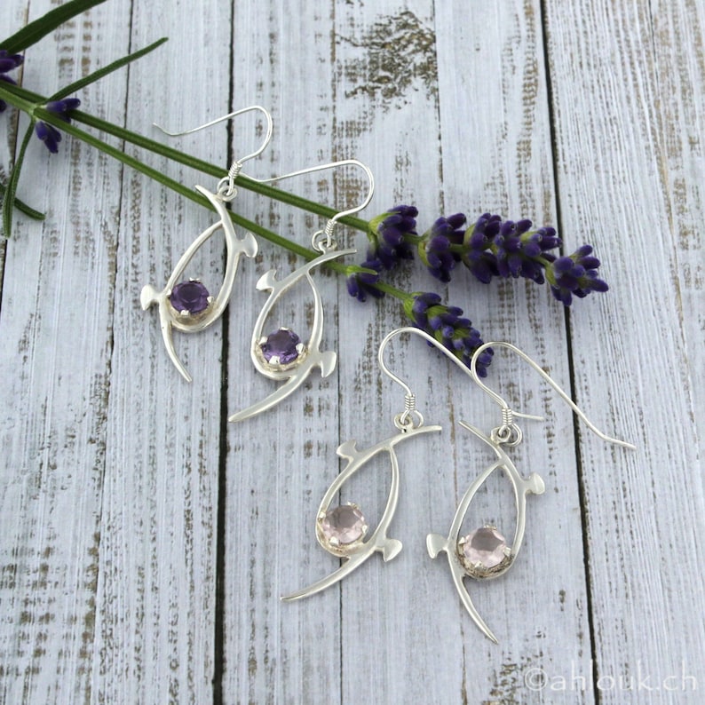 Pu&ograve; includere: Un paio di orecchini d'argento con delicati disegni di forma organica. Un orecchino presenta una pietra preziosa viola, mentre l'altro presenta una pietra preziosa rosa.