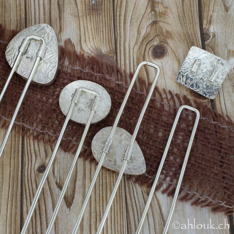 May include: Five silver bookmark pendants with intricate designs. Each pendant features a different design, including floral patterns and geometric shapes. The pendants are attached to silver metal rods.