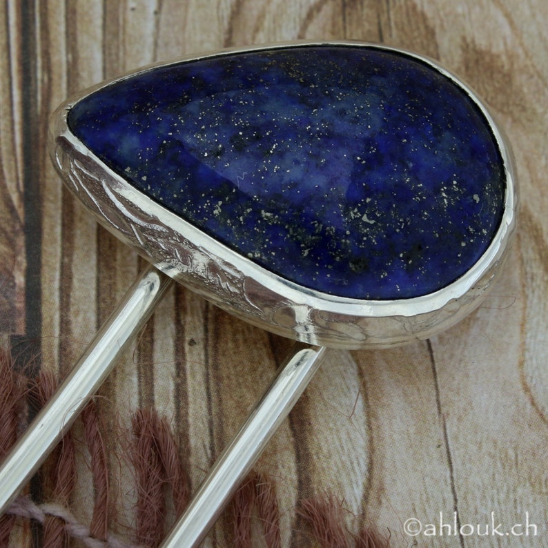 May include: A silver hair comb with a large, teardrop-shaped lapis lazuli stone set in the center. The stone has a deep blue color with flecks of gold pyrite.