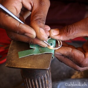 May include: A person's hands are working on a silver ring with a green gemstone. The ring is being set on a piece of green leather.