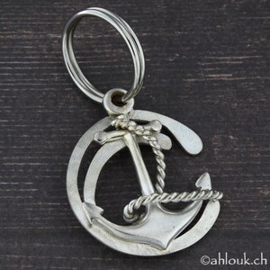 May include: A silver anchor keychain with a rope design. The anchor is surrounded by a circle with a textured pattern.
