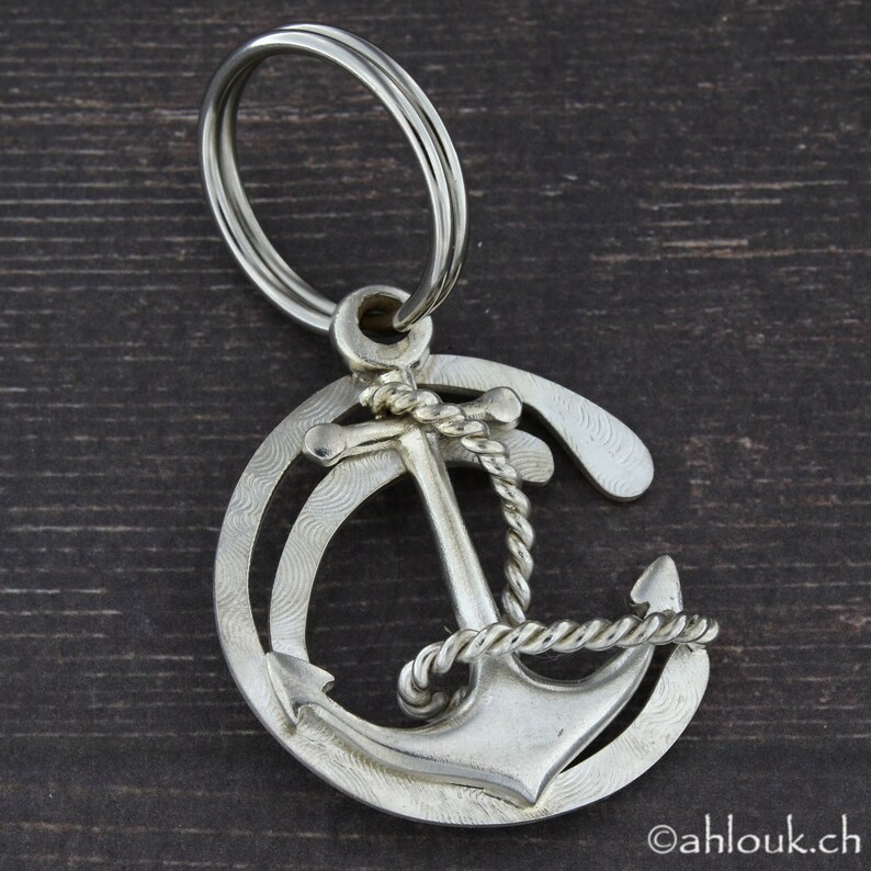 May include: A silver anchor keychain with a rope design. The anchor is surrounded by a circle with a textured pattern.
