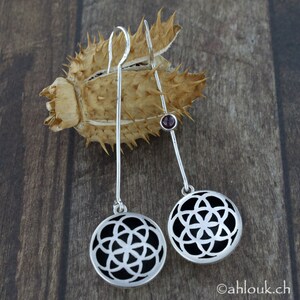 May include: A pair of silver earrings with a black geometric design and a small red gemstone accent.