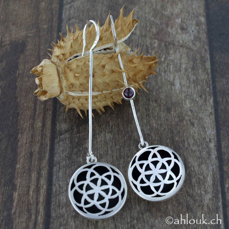May include: A pair of silver earrings with a black geometric design and a small red gemstone accent.