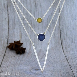 May include: A silver necklace with three chains and two gemstone pendants. The top pendant is a light green opal, and the bottom pendant is a dark blue stone. The chains are connected to a V-shaped silver pendant.