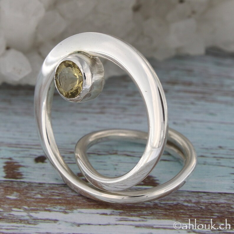 May include: A silver ring with a swirling design and a yellow gemstone set in the center.