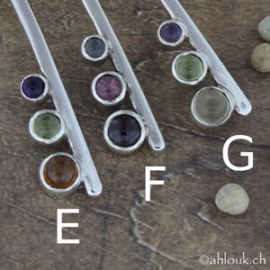 May include: Five silver bars with different colored gemstones set in them. The gemstones are purple, green, blue, pink, and brown. The bars are labeled E, F, and G.