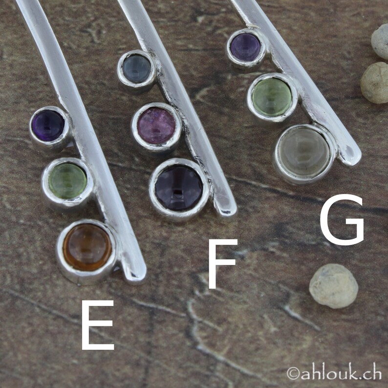 May include: Five silver bars with different colored gemstones set in them. The gemstones are purple, green, blue, pink, and brown. The bars are labeled E, F, and G.