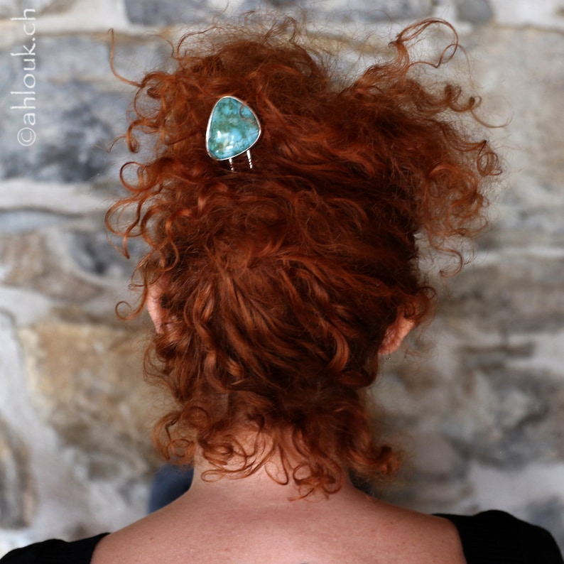 May include: A woman with curly red hair is wearing a turquoise gemstone hair clip. The clip is silver and has a simple design.