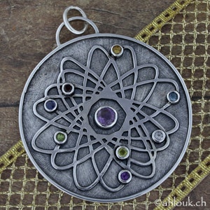 May include: A silver pendant with a circular design featuring a central amethyst gemstone surrounded by smaller gemstones in various colors, including green, blue, and yellow. The pendant has a delicate, intricate pattern that resembles a stylized atom.