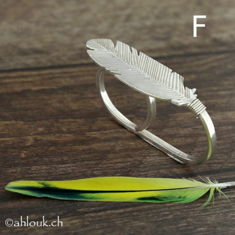 May include: A silver feather ring with two bands. The ring is designed to be worn on two fingers. The feather is detailed and textured.
