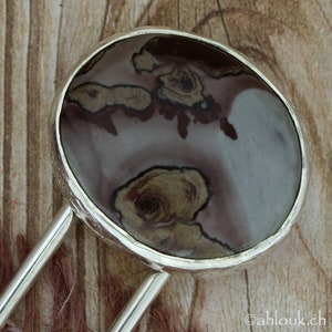 May include: A silver pendant with a round, brown, white, and gray stone with a swirling pattern. The stone is set in a silver bezel.