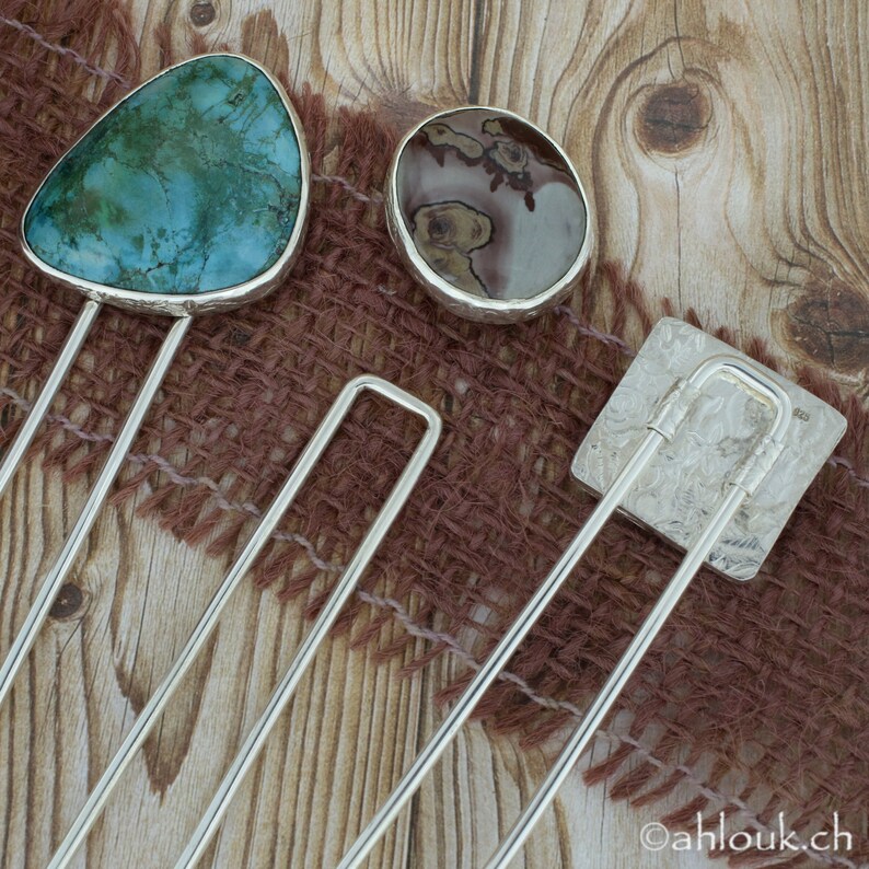 May include: Three silver hair clips with different gemstone accents. The first clip features a turquoise stone, the second a brown and white stone, and the third a silver square with a textured design.