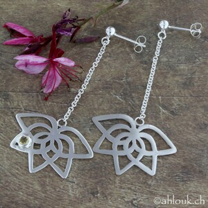 May include: A pair of silver dangle earrings with a delicate floral design. Each earring features a small, round, yellow gemstone.