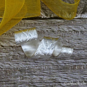 May include: A silver, twisted, and textured ring with a floral design. The ring is on a wooden surface.