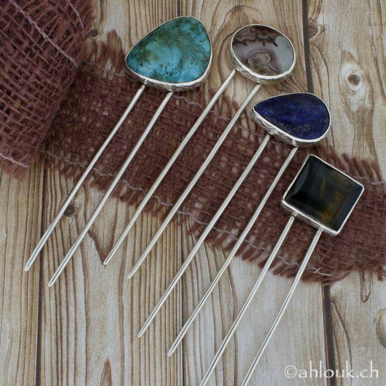 May include: Five silver hair sticks with different colored gemstone tops. The tops are turquoise, brown, blue, and black.