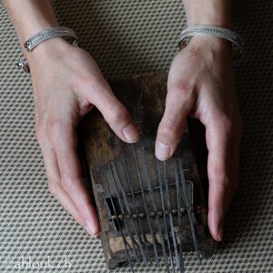 Puede incluir: Un instrumento musical de madera con l&aacute;minas de metal, conocido como kalimba, est&aacute; siendo tocado por una persona con pulseras de plata en ambas mu&ntilde;ecas.