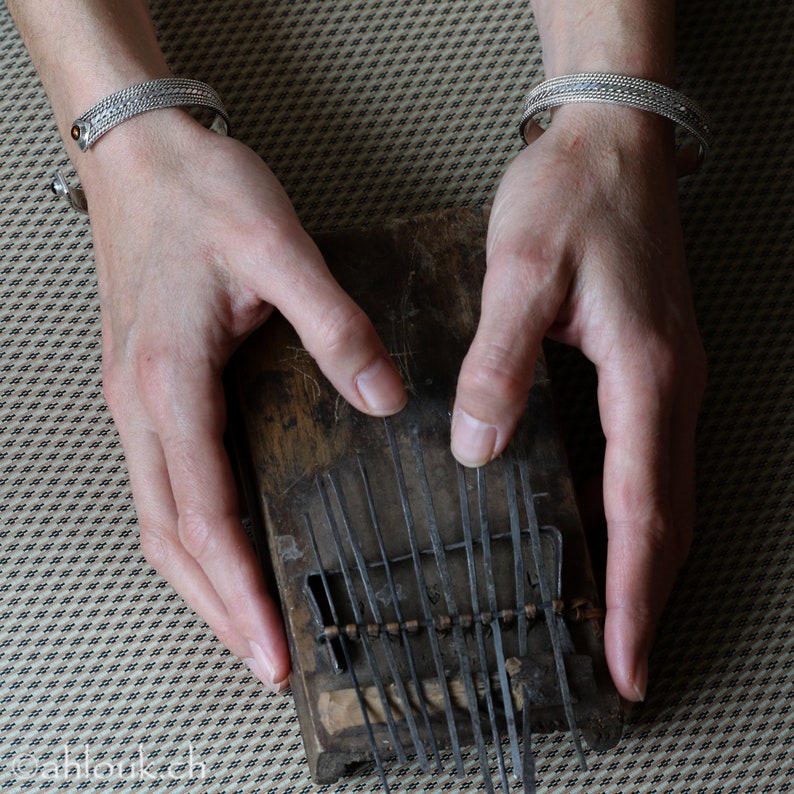 Puede incluir: Un instrumento musical de madera con l&aacute;minas de metal, conocido como kalimba, est&aacute; siendo tocado por una persona con pulseras de plata en ambas mu&ntilde;ecas.