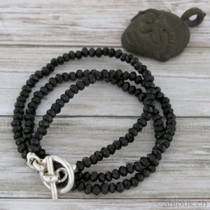 May include: A black beaded necklace with a silver toggle clasp. The necklace is made of faceted beads and is layered for a stylish look.