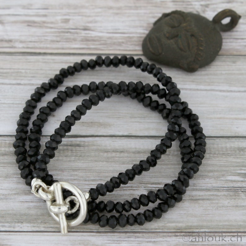 May include: A black beaded necklace with a silver toggle clasp. The necklace is made of faceted beads and is layered for a stylish look.