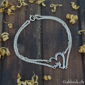 May include: A silver chain bracelet with a heart-shaped charm featuring a puzzle piece design. The bracelet is double-stranded and has a lobster clasp closure.