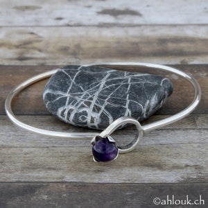May include: A silver bangle bracelet with a purple amethyst gemstone set in a floral design.