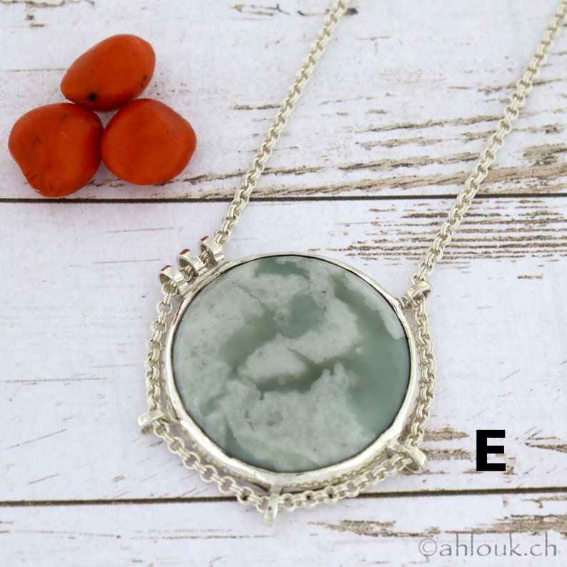 Puede incluir: Un collar de cadena de plata con un colgante redondo con una piedra de &aacute;gata verde y blanca. El colgante est&aacute; engastado en un marco de plata con un dise&ntilde;o decorativo. La letra "E" es visible en la esquina inferior derecha de la imagen.