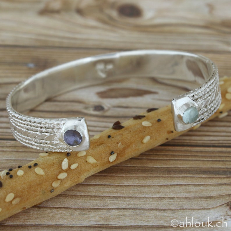 Puede incluir: Pulsera de plata con un dise&ntilde;o tejido y dos piedras redondas. Una piedra es azul y la otra es azul claro.