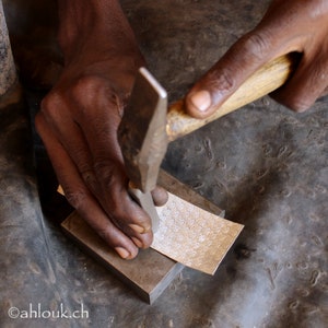 May include: A person uses a hammer to stamp a design into a silver sheet. The sheet has a repeating pattern of small circles.