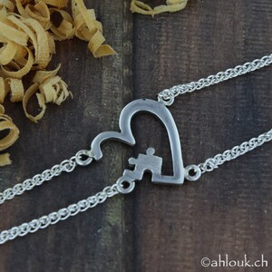 May include: Two silver chain bracelets with a heart-shaped charm. The heart is cut out and has a puzzle piece inside. The puzzle piece is also cut out.