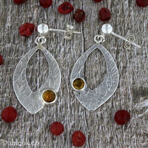 May include: Silver dangle earrings with a delicate leaf pattern and two round, yellow gemstones.