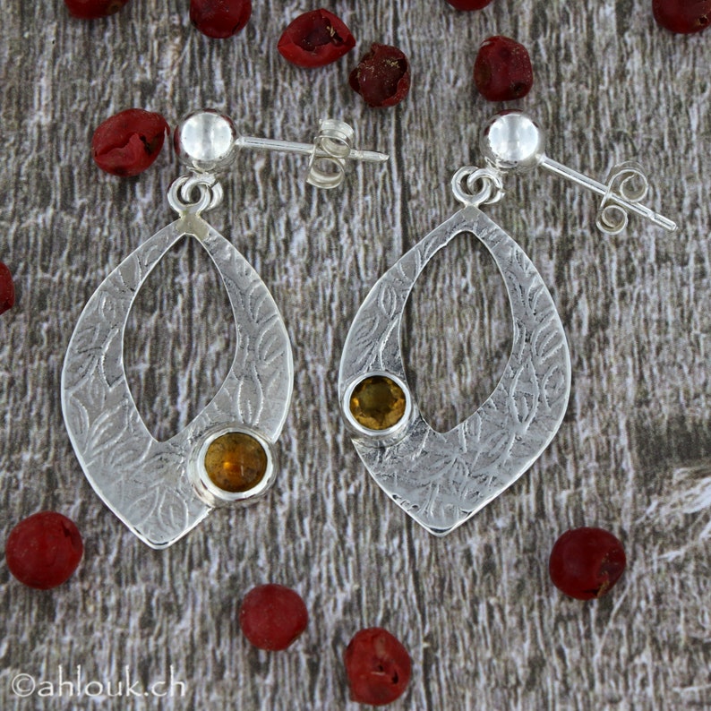 May include: Silver dangle earrings with a delicate leaf pattern and two round, yellow gemstones.