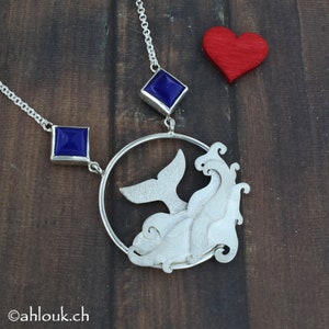 May include: A silver necklace with a whale tail and wave design pendant. The pendant is surrounded by a circle and features two blue gemstone accents.