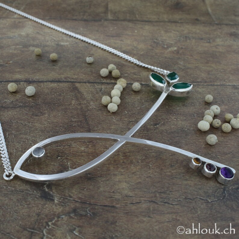 May include: A silver necklace with a fish pendant and a green leaf design. The pendant is adorned with small gemstones in various colors.