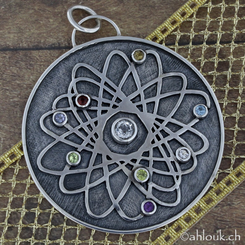 May include: A silver pendant with a detailed atom design and colorful gemstones. The pendant is round and has a textured surface.