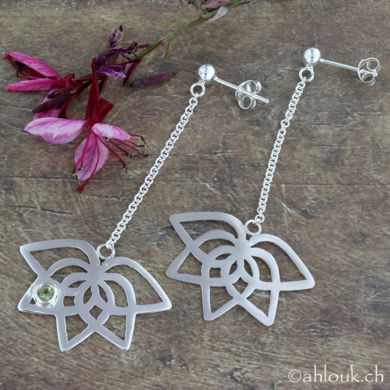 May include: A pair of silver dangle earrings with a delicate chain and a detailed floral design. Each earring features a small green gemstone in the center of the flower.