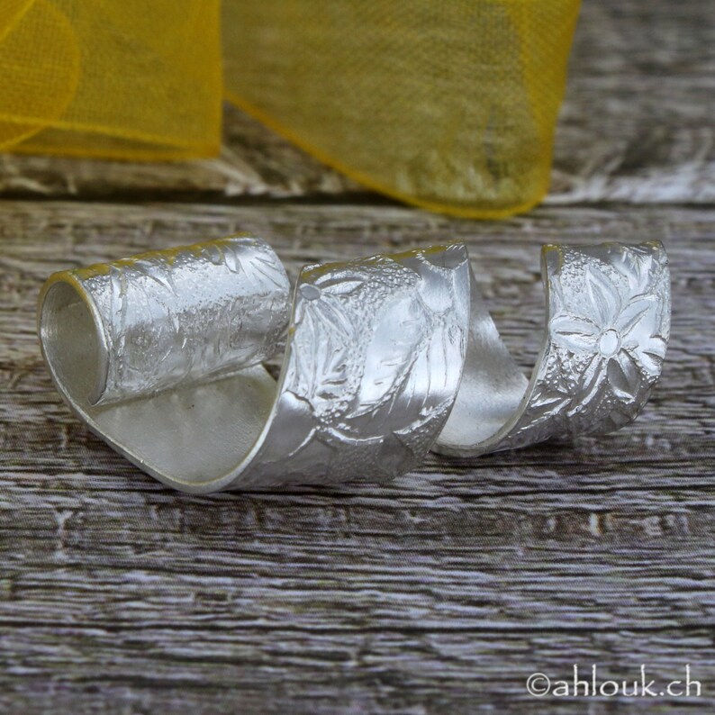 May include: A silver ring with a floral design. The ring is twisted and has a textured surface.