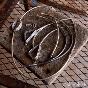 Peut inclure: Un ensemble de bijoux en m&eacute;tal argent&eacute;, comprenant un grand cercle, deux formes triangulaires et deux petits cercles, dispos&eacute;s sur une surface textur&eacute;e grise.