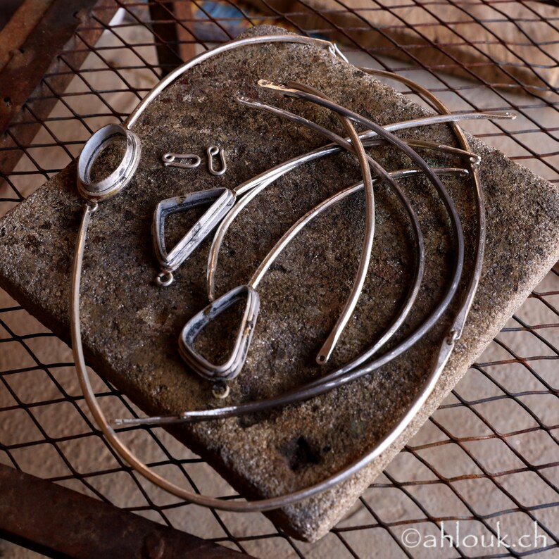 Peut inclure: Un ensemble de bijoux en m&eacute;tal argent&eacute;, comprenant un grand cercle, deux formes triangulaires et deux petits cercles, dispos&eacute;s sur une surface textur&eacute;e grise.