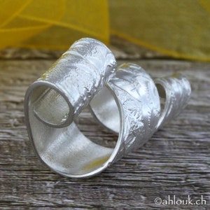 May include: A silver ring with a textured, swirling design. The ring is made of metal and has a polished finish.
