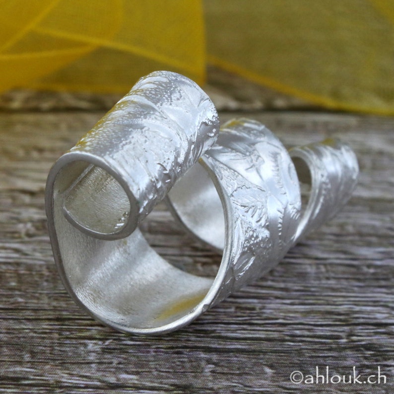 May include: A silver ring with a textured, swirling design. The ring is made of metal and has a polished finish.