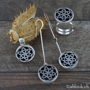 May include: A set of silver earrings and a ring featuring a geometric design with a black center. The earrings are dangle style with a small black stone on the top of the dangle. The ring is a double band with a wide top.