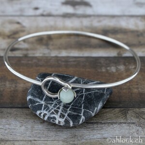 May include: A silver bangle bracelet with a light green stone accent. The bracelet is open and has a simple design.